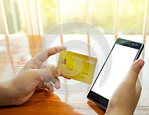 Online shopping concept with human hand holding smart phone and credit card on wood table and window background