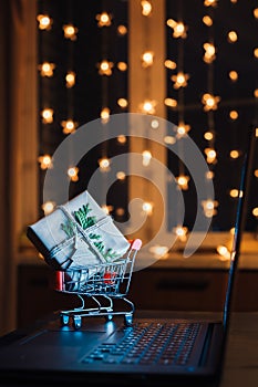 Online shopping concept. Miniature shopping cart with gift box on laptop