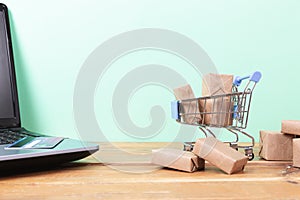 Online shopping concept. Shopping cart, small boxes, laptop and credit card on the desk