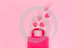 Online shopping concept. Top view of gift bag and pink paper hearts on pink background with ripple effect, copy