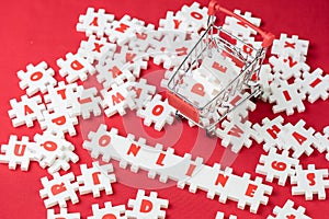 Online shopping concept, white puzzle jigsaws with alphabets building the word Online with shopping cart or trolley on red fabric