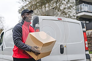 Online shopping delivery concept. Positive smiling Black man in his late 20s holding big cardboard package. Medium
