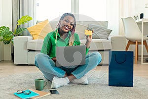 Online shopping and delivery. Excited african american lady showing credit card using laptop, advertising sales offer