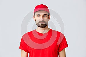 Online shopping, delivery during quarantine and takeaway concept. Young handsome bearded courier in red service uniform