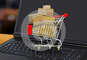 Online shopping and delivery service concept with shopping cart full of boxes on laptop