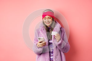 Online shopping and fashion concept. Stylish asian elderly woman standing in fashionable purple coat and making payment