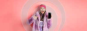 Online shopping and fashion concept. Stylish asian senior woman in faux fur coat pointing finger at blank smartphone