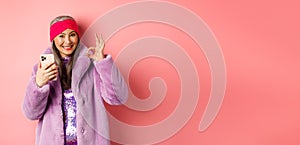 Online shopping and fashion concept. Stylish asian senior woman showing okay sign and holding mobile phone, recommending
