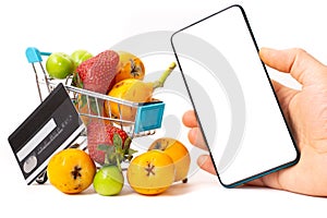 Online shopping for fruits and vegetables, fruits in a shopping cart, credit card and blankscreen copyspace smartphone with white