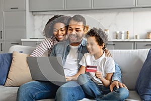 Online Shopping. Happy Black Family Using Laptop And Credit Card At Home