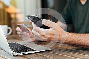 Online shopping from home balcony, man using laptop, mobile smart phone and credit card to purchase