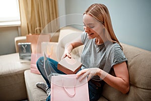 Online shopping at home. Young excited woman is unboxing her parcel, ordered by internet, while sitting on the sofa