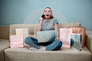 Online shopping at home. Young surprised woman with credit card is ready to Singles day on a sofa near shopping bags