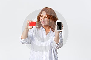 Online shopping, internet banking and money transfer concept. Impressed and amused redhead middle-aged woman looking