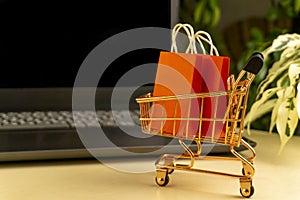 online shopping . little shopping cart with colorful shopping bags inside stand near laptop, little deliver boxes, bank ca