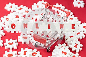 Online shopping metaphor, white puzzle jigsaws with alphabets building the word Online on shopping cart or trolley on red fabric