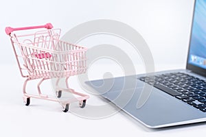 Online shopping. Mini empty pink shop cart trolley over a laptop computer on white table background, buying at home concept, close