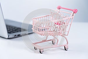 Online shopping. Mini empty pink shop cart trolley over a laptop computer on white table background, buying at home concept, close