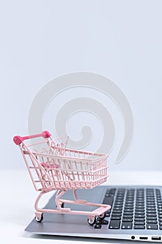 Online shopping. Mini empty pink shop cart trolley over a laptop computer on white table background, buying at home concept, close