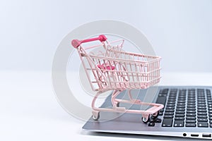 Online shopping. Mini empty pink shop cart trolley over a laptop computer on white table background, buying at home concept, close