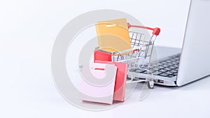 Online shopping. Mini shop cart trolley with colorful paper bags over a laptop computer on white table background, buying at home