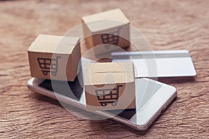Online shopping - Paper cartons or parcel with a shopping cart logo and credit card, smartphone on wood table top. Shopping