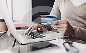 Online shopping. Young woman holding credit card and using laptop at home. African american girl working on computer at cafe.