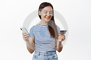 Online shopping. Young woman paying with credit card and mobile phone, smiling and looking relaxed, purchase smth in