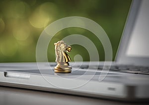 Online strategy, online marketing or business strategy concept. Golden chess knight is on laptop with bokeh background depth of