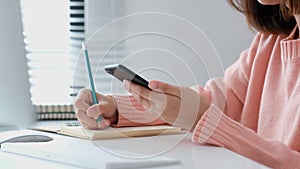 Online study, Woman hand writing on notebook while using mobile phone for digital home study class, Adult female student doing