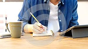 Online studying class, Student man hand writing on notebook while using digital tablet for e learning, Adult male university,
