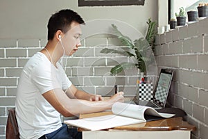 Online studying concept the high school student listening to music through his earphones and using his laptop to search