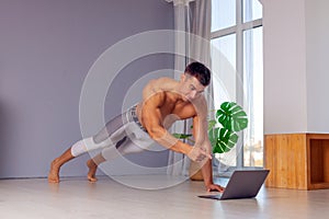 Online trainer. On-line sports. fitness and healthy lifestyle concept. Man with laptop computer doing plank exercise at