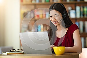 Online Tutoring. Asian Woman Tutor With Headset Working On Laptop In Cafe
