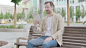 Online Video Chat on Tablet by Young Man Sitting on Bench