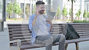 Online Video Chat on Tablet by Young Man Sitting on Bench