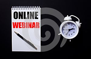 ONLINE WEBINAR is written in a white notepad near a white alarm clock on a black background