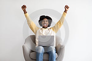 Online Win. Happy Black Guy Celebrating Success With Laptop, Sitting In Chair