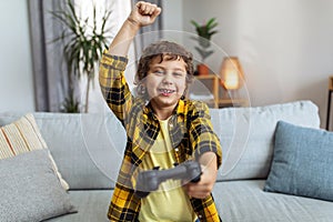 Online win. Happy little boy gamer with joystick celebrating victory in video game, laughing and gesturing to camera