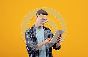 Online work, communiction, education. Cool young man browsing web on tablet pc over orange studio background