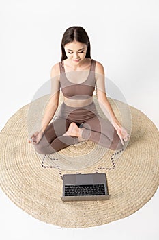 Online yoga lessons. Asian woman sitting in lotus pose against the laptop.