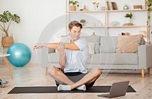 Online yoga lessons. Smiling man doing warm up and sits in lotus pose on mat