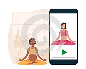 Online yoga. Pregnant African American woman sitting in lotus position on mat at home. Woman watches at yoga lessons on