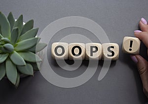 Oops symbol. Concept word Oops on wooden cubes. Businessman hand. Beautiful grey background with succulent plant. Business and