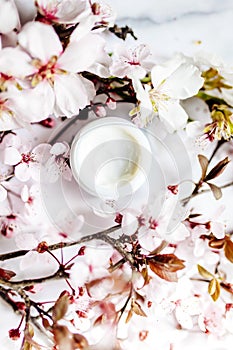 op view of cosmetic cream with pink cherry flowers in a blue glass jar. Hygienic skincare lotion product.Idioma de palabras photo