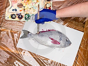 Op view of gloved hand paints fins of raw fish