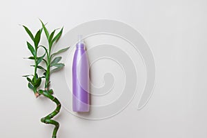 Opaque cosmetic bottle lying near bamboo on light yellow background with copy space