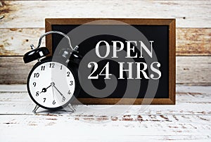 Open 24 HRS text message with alarm clock on wooden background