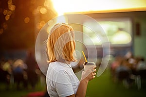 Open-air cinema. Girl with a glass of coffee watching a movie in a summer cinema