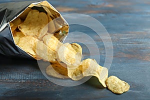 Open bag with crispy potato chips on color wooden table